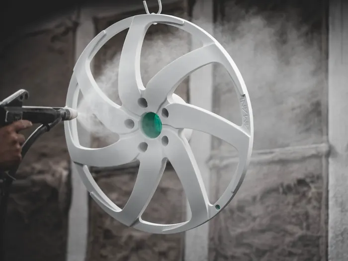 A gloved hand spraying powder onto a bare wheel face hanging from a hook